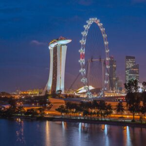 Stunning night view of Singapore with Marina Bay Sands and Ferris Wheel, reflecting city lights on water.